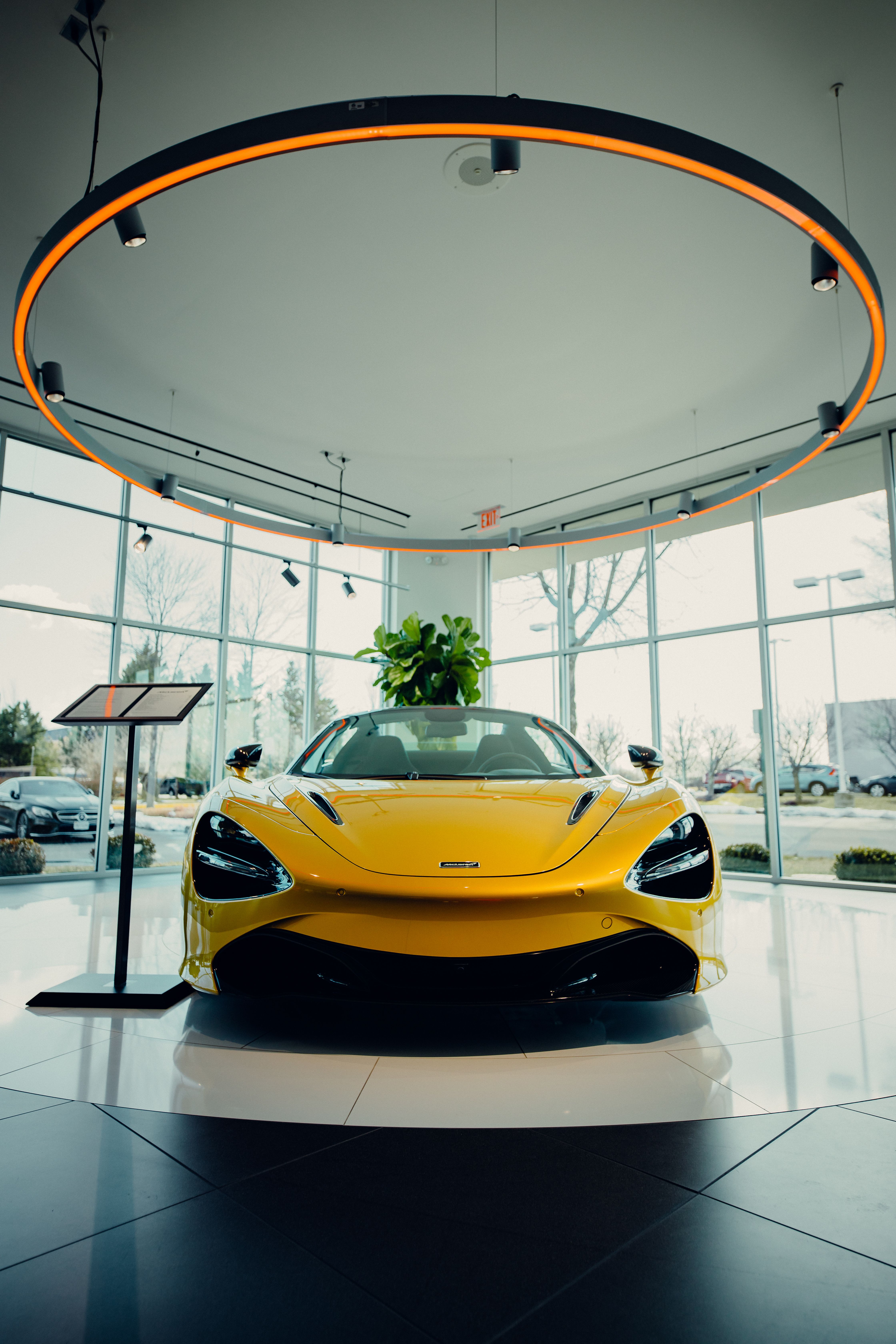 Yellow sports car displayed beneath circular lighting inside a glass-fronted dealership