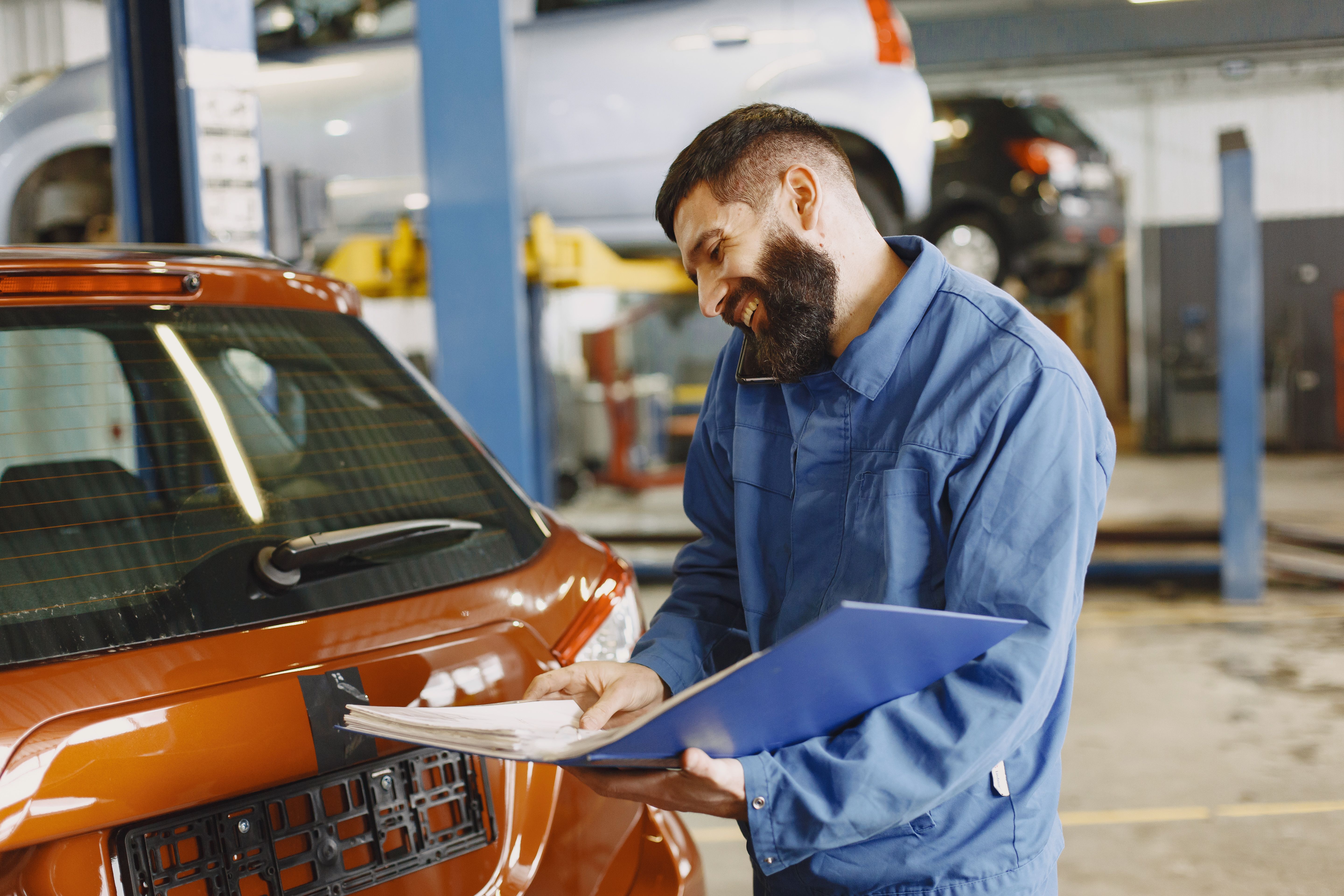 Smiling service technician reviewing paperwork beside a car in the workshop
